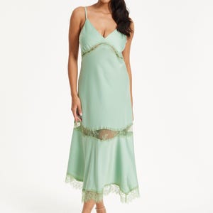 Peut inclure: Robe de style nuisette vert clair avec fines bretelles et décolleté en V. La robe est ornée de dentelle au niveau de l'encolure, du milieu et de l'ourlet. La modèle porte des talons nude.