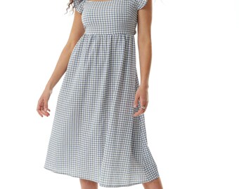 May include: A light blue and white gingham midi dress with a square neckline and short, ruffled sleeves. The dress has a fitted bodice and a flared skirt. The model is wearing white strappy heels.