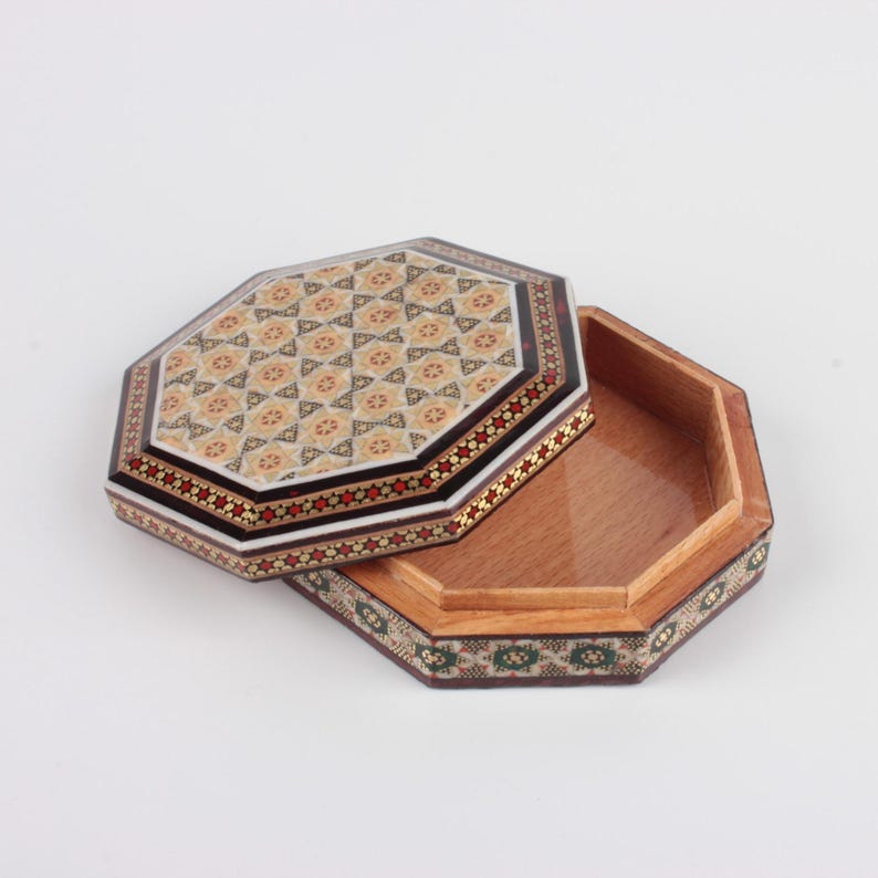 May include: An open, octagonal wooden box with a decorative lid. The lid features a mosaic pattern with beige, red, and black accents. The box's interior is a light brown, and the edges are adorned with intricate designs.