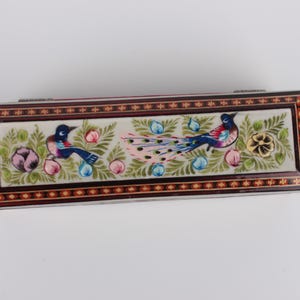May include: A rectangular wooden box with a hinged lid, decorated with intricate floral and bird designs. The box is painted with vibrant colors, including blue, green, pink, and gold. The lid features a peacock with its tail feathers spread out, surrounded by flowers and birds.