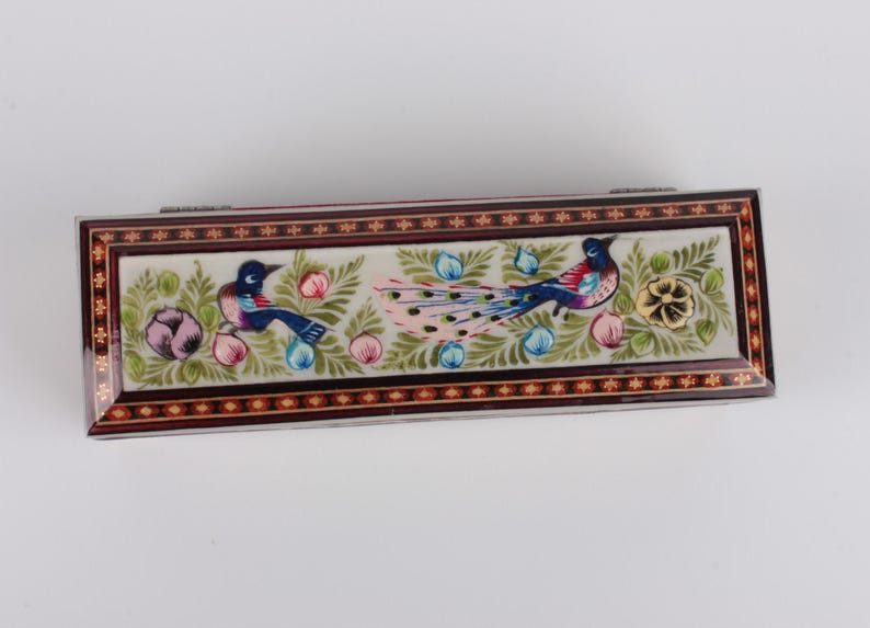 May include: A rectangular wooden box with a hinged lid, decorated with intricate floral and bird designs. The box is painted with vibrant colors, including blue, green, pink, and gold. The lid features a peacock with its tail feathers spread out, surrounded by flowers and birds.