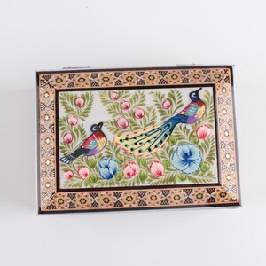 May include: A rectangular decorative box featuring a hand-painted scene of two birds amidst green foliage, pink flower buds, and blue blossoms. The border displays a geometric pattern in black, gold, and white, framing the central illustration.