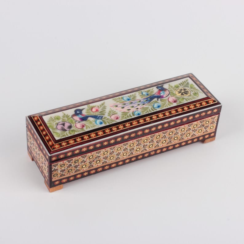May include: A rectangular wooden box with a hinged lid. The lid is decorated with a colorful floral design and two peacocks. The box is made of inlaid wood and has a dark brown finish.