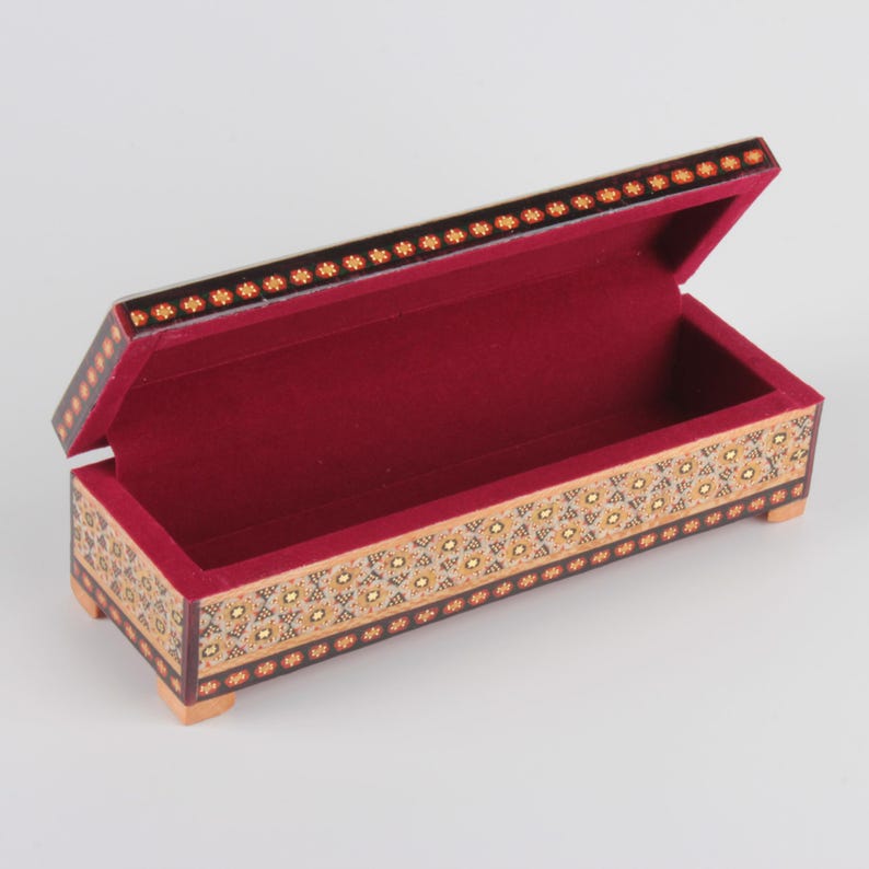 May include: A rectangular wooden box with a red velvet interior. The box is decorated with intricate geometric patterns in gold, black, and white.