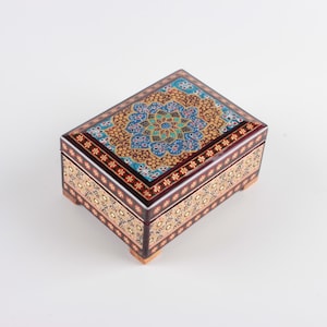 May include: A rectangular wooden box featuring intricate hand-painted floral and geometric patterns in shades of blue, gold, red, and black. The lid displays a central mandala-like design, while the sides are decorated with repeating flower motifs.