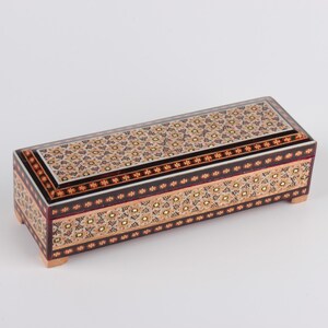 May include: A rectangular wooden box with intricate inlaid designs in shades of brown, gold, and white. The box has a hinged lid and is decorated with a geometric pattern.