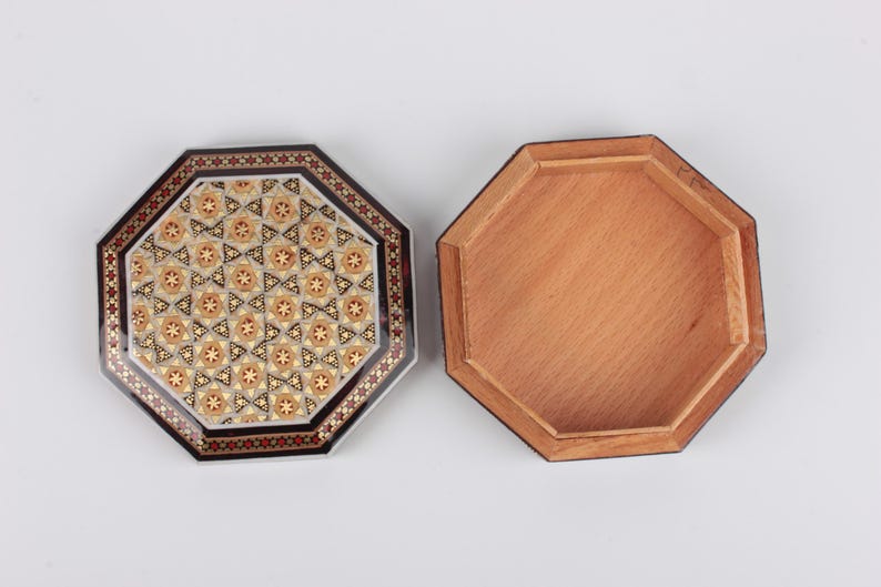 May include: An open, octagonal wooden box with a decorative lid. The lid features a detailed mosaic pattern in shades of brown, beige, and black. The box's interior is a light brown color, and the box is set against a white background.