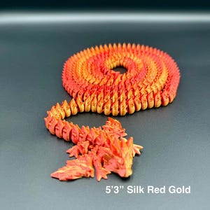 May include: A 5'3" Silk Red Gold dragon figurine, coiled and posed. The dragon is a gradient of red and gold, with a detailed, textured surface. The dragon is a fantasy-themed item.