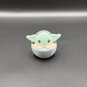 May include: Three Star Wars character figurines: a white Stormtrooper, a green Grogu in a gray carrier, and a gray Darth Vader. Each figure has a unique design and stands on a dark surface. The figurines are approximately 3 inches tall.