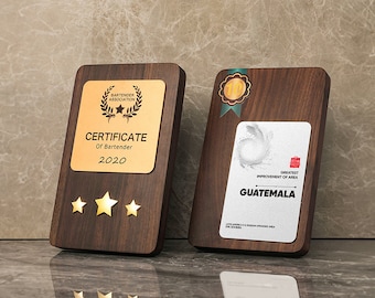 Puede incluir: Dos placas de madera con detalles dorados. La placa de la izquierda tiene un certificado dorado con el texto "CERTIFICATE of Bartender 2020" y tres estrellas doradas. La placa de la derecha tiene una medalla dorada con el número "1" y una placa plateada con el texto "GREATEST IMPROVEMENT OF AREA GUATEMALA".