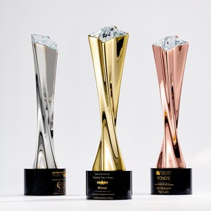 May include: Three awards with a twisted metal design and a crystal top. The awards are silver, gold, and copper-coloured, each on a black base with text. The awards are for real estate achievements.