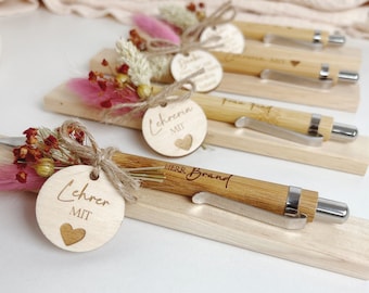 May include: Four wooden pen holders with bamboo pens and dried flowers. Each pen holder has a personalized wooden tag with the text "Lehrer mit" and a heart. The pens are engraved with the text "Herr Brand".