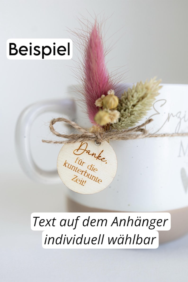 Op de afbeelding: Witte keramische mok met een arrangement van gedroogde bloemen en een houten label. Het label leest "Danke, f&uuml;r die kunterbunte Zeit!" en is vastgebonden met touw. De tekst "Text auf dem Anh&auml;nger individuell w&auml;hlbar" is ook zichtbaar.