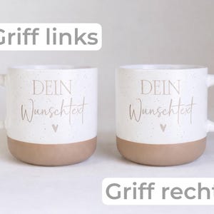 May include: Two white ceramic mugs with speckled details and a tan base. Each mug features the text "DEIN Wunschtext" and a small heart icon. One mug has a handle on the left, and the other has a handle on the right. The text "Griff links" and "Griff rechts" appear above and below the mugs.