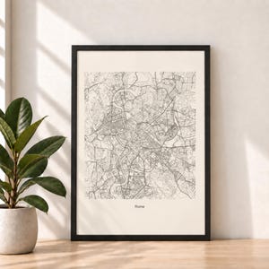 Puede incluir: Una lámina enmarcada que muestra un mapa detallado de líneas negras de Roma sobre un fondo crema. El mapa exhibe el intrincado trazado de las calles y el sinuoso río Tíber. La palabra Rome está impresa en letras negras pequeñas abajo al centro.