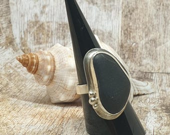 Puede incluir: Un anillo de plata con una piedra negra engastada en un engaste de plata. El anillo está en un expositor de anillos negro.