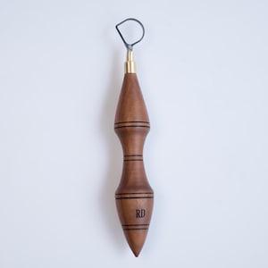 May include: A wooden pottery rib tool with a brass ferrule and a looped wire end. The handle is a dark brown color with engraved lines and the initials "RD". The tool is designed for shaping and smoothing clay.