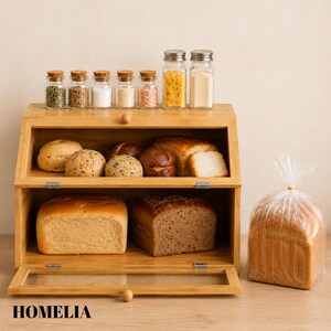 May include: A wooden bread bin with a glass door, containing different loaves and rolls. Small glass jars with cork and metal lids hold spices. A loaf of sliced bread is in a plastic bag. The word "HOMELIA" is at the bottom.
