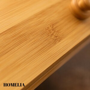 May include: Close-up of a bamboo cutting board with visible wood grain. The board is a light brown colour and has the word "HOMELIA" printed on the bottom left corner. The surface is smooth and appears to be well-crafted.