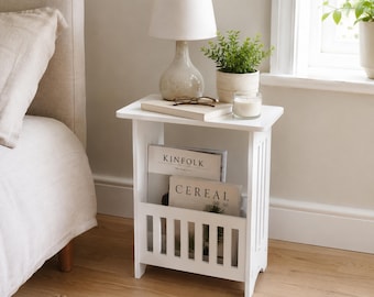May include: A white wooden side table with a lamp, plant, and books. The table features a magazine rack with the words "KINFOLK" and "CEREAL". A candle and glasses are on the tabletop. The word "HOMELIA" is at the bottom.