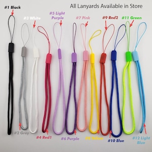 May include: A selection of 12 different colored lanyards, each with a loop at the top. The lanyards are arranged in a row from left to right, with the colors black, grey, white, red, light purple, purple, pink, yellow, red, blue, green, and light blue.