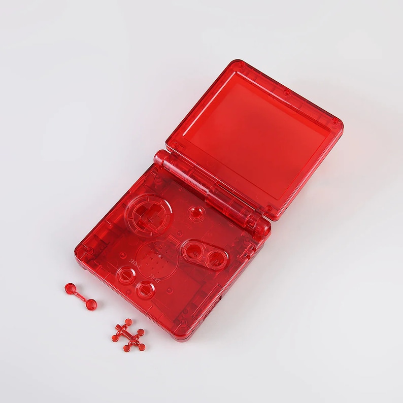 May include: A red transparent Game Boy Advance SP shell with buttons and a screen. The shell is open and the screen is visible. There are also some small red plastic pieces.