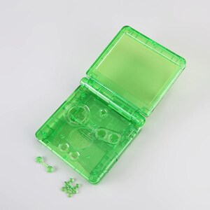May include: A transparent green handheld game console shell with buttons and a screen. The shell is open and the screen is facing up. There are small plastic pieces scattered around the shell.