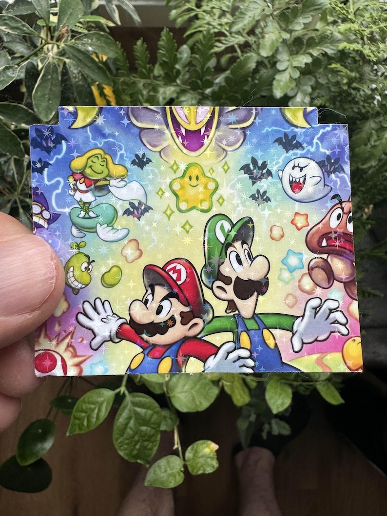 May include: A colorful card featuring Mario and Luigi from the Super Mario Bros. video game series. The card has a blue background with stars, bats, and other characters from the game.