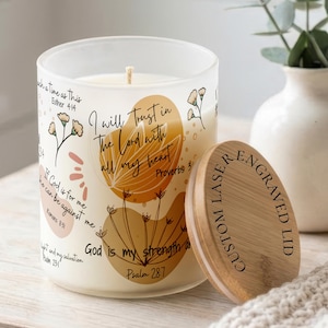 May include: A frosted glass candle jar featuring orange and tan abstract floral illustrations and black text including Bible verses. The jar has a light-colored wooden lid with the laser-engraved text CUSTOM LASER ENGRAVED LID.