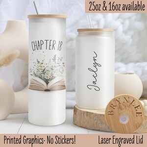 May include: Two white tumblers with lids and straws. The tumbler on the left has a floral design and the text "CHAPTER 18". The tumbler on the right has the name "Jaclyn" written on it. The lid on the right tumbler is a laser engraved wooden lid with the name "BRYNLEE".
