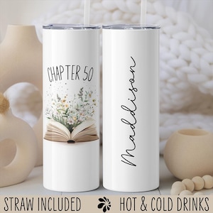 May include: White stainless steel tumbler with a black straw. The tumbler has a floral design and an open book with the text "Chapter 50". The other tumbler has the name "Madison" written vertically on it.