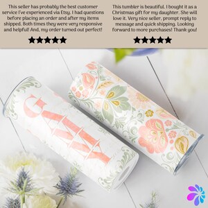 May include: Two stainless steel tumblers with a floral pattern. One tumbler has the word "Grateful" written in pink on the front. The tumblers are on a white wooden surface.