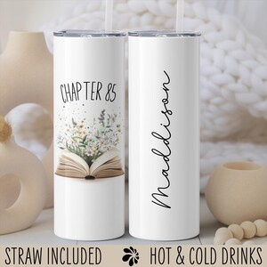 May include: White stainless steel tumbler with a black and white design. The tumbler features a book with flowers coming out of it and the text "Chapter 85". The other tumbler has the name "Madison" written vertically on it.