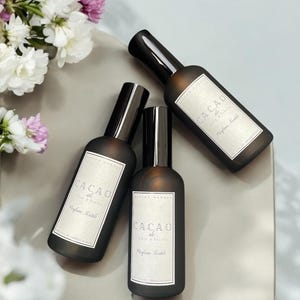 Puede incluir: Tres botellas de vidrio marrón con tapas negras y etiquetas blancas. Las etiquetas dicen "Cacao de Costa de Marfil Parfum Textile".