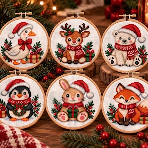 Peut inclure: Six tambours à broder circulaires en bois présentant des motifs au point de croix d'une oie, d'un renne, d'un ours polaire, d'un pingouin, d'un lapin et d'un renard. Chaque animal porte un bonnet et une écharpe rouges, entouré de houx.