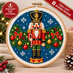 Puede incluir: Un patrón de punto de cruz en un bastidor de madera que muestra un soldado cascanueces con uniforme rojo sobre fondo azul, rodeado de ramas de pino, adornos rojos y dorados y copos de nieve blancos, con el texto INSTANT PDF PATTERN.
