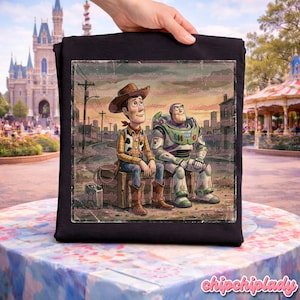 May include: Black t-shirt featuring a vintage-style illustration of Woody and Buzz Lightyear from Toy Story. Woody is in a cowboy outfit, and Buzz is in his space suit. They are sitting on a wooden crate with a sunset background.