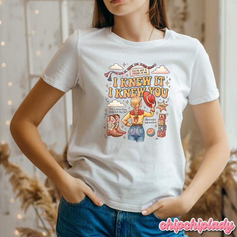 May include: A white short-sleeved t-shirt featuring a colourful graphic print. The design includes a cartoon character with blonde hair, a red hat, and cowboy boots, surrounded by text reading I KNEW IT I KNEW YOU, YOU'VE GOT A FRIEND IN ME.