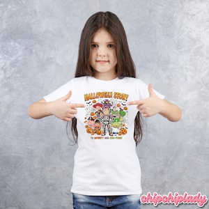 May include: White t-shirt with a colorful Halloween-themed graphic. The graphic features characters from the movie Toy Story, including Woody, Buzz Lightyear, and others, in Halloween costumes. The text "HALLOWEEN STORY" and "TO INFINITY AND BOO-YOND!" are also included.