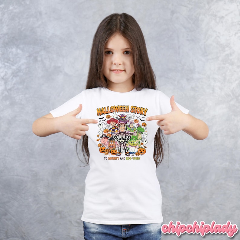 May include: White t-shirt with a colorful Halloween-themed graphic. The graphic features characters from the movie Toy Story, including Woody, Buzz Lightyear, and others, in Halloween costumes. The text "HALLOWEEN STORY" and "TO INFINITY AND BOO-YOND!" are also included.