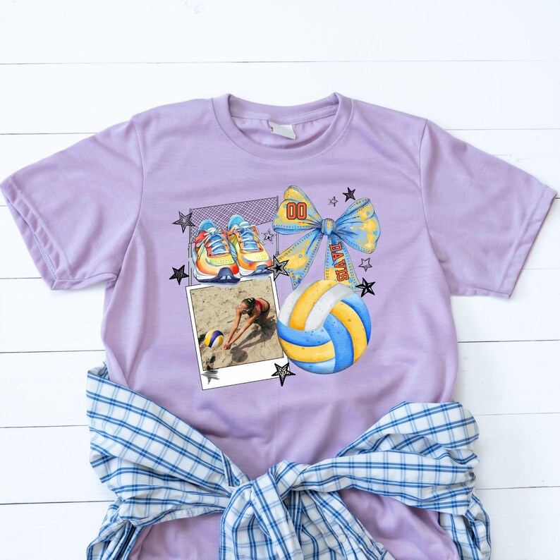 May include: Purple t-shirt with a volleyball graphic. The graphic features a volleyball, a bow with the word "PLAYER" on it, a pair of sneakers, and a photo of a volleyball player. The graphic is surrounded by stars.