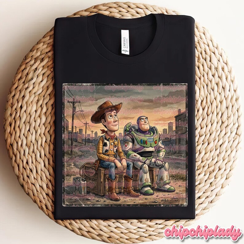 May include: Black t-shirt featuring a distressed graphic of Woody and Buzz Lightyear from Toy Story. Woody is in a cowboy outfit, and Buzz is in a spacesuit. The graphic is set against a cityscape backdrop.