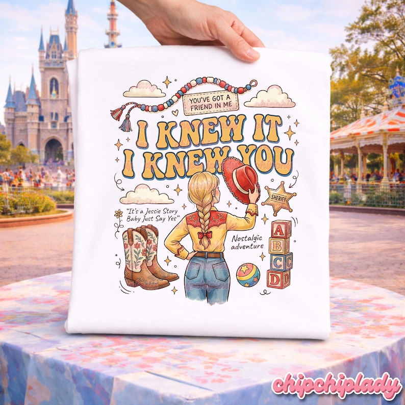 May include: A white t-shirt featuring a colourful graphic illustration of a cowgirl with a braided ponytail, holding a red hat. The design includes cowboy boots, a sheriff badge, alphabet blocks, a ball, and text reading I KNEW IT I KNEW YOU.