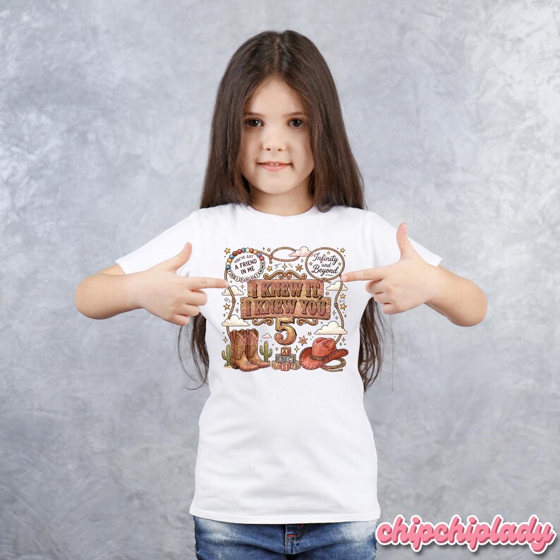 May include: A white short-sleeved t-shirt featuring a western-themed graphic with the text "I KNEW IT, I KNEW YOU" and the number "5". The design includes a cowboy hat, cowboy boots, a lasso, cacti, and clouds, with "A FRIEND IN ME" text.