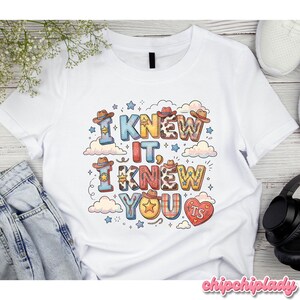 K&ouml;nnte beinhalten: Ein wei&szlig;es Kurzarm-T-Shirt mit einem farbenfrohen Grafikdruck mit dem Text I KNEW IT, I KNEW YOU. Das Design enth&auml;lt verschiedene Elemente im Western-Stil wie Cowboyh&uuml;te, Sterne, Kuhfellmuster und ein rotes Herz mit der Aufschrift TS.