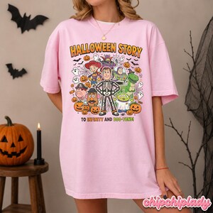 May include: A light pink t-shirt with a colorful graphic featuring characters and pumpkins. The text "HALLOWEEN STORY" is above the characters, and "TO INFINITY AND BOO-YOND!" is below. The shirt is a Halloween-themed item.