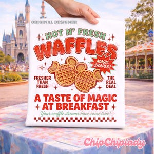 K&ouml;nnte beinhalten: Ein wei&szlig;es T-Shirt mit einem Grafikdruck mit dem Text HOT N' FRESH WAFFLES, MAGIC SHAPED, FRESHER THAN FRESH, THE REAL DEAL, A TASTE OF MAGIC AT BREAKFAST und Your waffle dreams have come true, sowie zwei mausf&ouml;rmigen Waffeln.