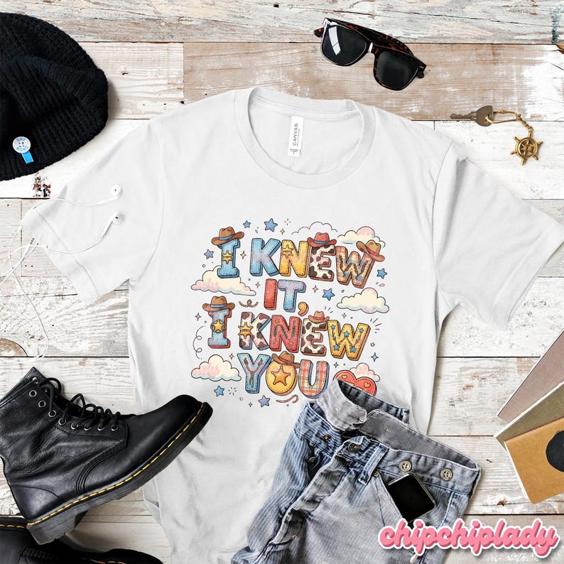 K&ouml;nnte beinhalten: Ein wei&szlig;es Kurzarm-T-Shirt mit einem farbenfrohen Grafikdruck und dem Text I KNEW IT, I KNEW YOU. Das Design enth&auml;lt verschiedene Western-Elemente wie Cowboyh&uuml;te, Sterne und Kuhfellmuster, die von kleinen Wolken umgeben sind.