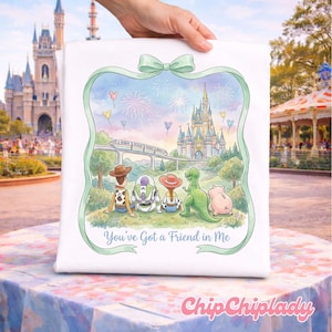 May include: White square cushion with a colourful illustration of Toy Story characters in front of a castle, fireworks, and a monorail. The image is framed by a green ribbon with a bow. Text reads "You've Got a Friend in Me".