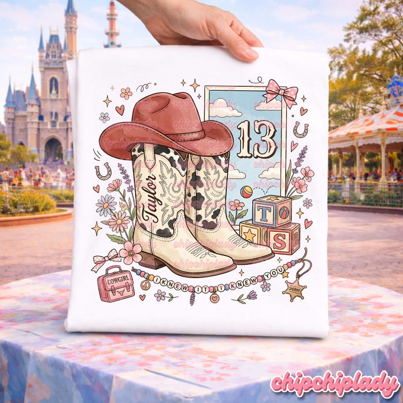 Pode incluir: Uma t-shirt branca com uma ilustra&ccedil;&atilde;o gr&aacute;fica de um chap&eacute;u de cowboy castanho sobre um par de botas de cowboy creme e pretas com padr&atilde;o de vaca. O design inclui o nome Taylor, o n&uacute;mero 13, blocos de letras, flores e o texto I KNEW IT I KNEW YOU.
